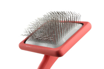 Red handled slicker brush with fine metal pins on a white background