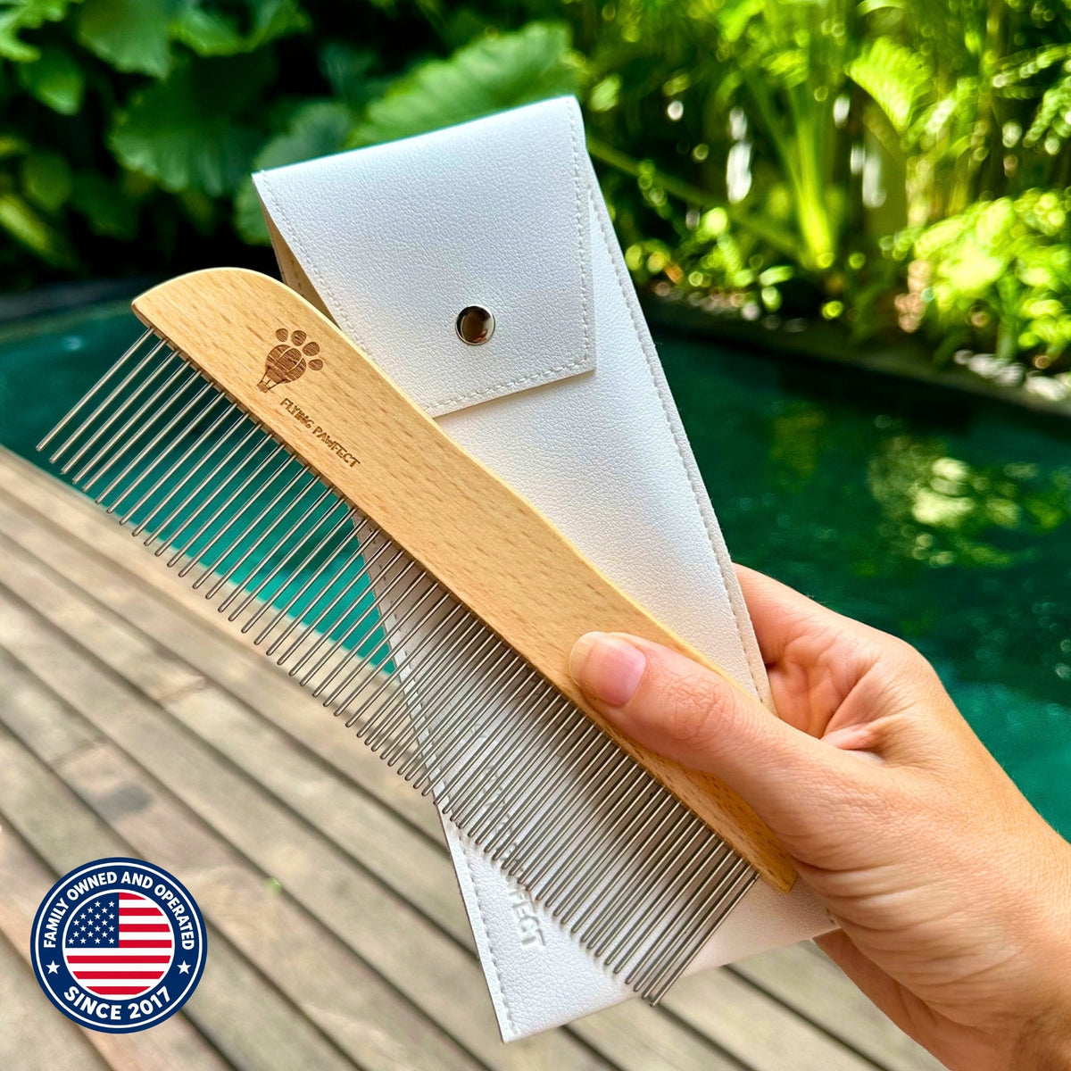 A hand holding the Flying Pawfect Long Tooth Comb and its white pouch beside a swimming pool